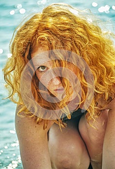 Beautiful portrait of a young elegant sexy red-haired curly woman sitting at the beach