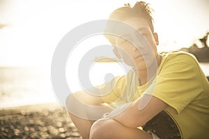 Beautiful portrait young handsome people male teenager looking at the camera sitting at the beach with sunset sun in backlight -