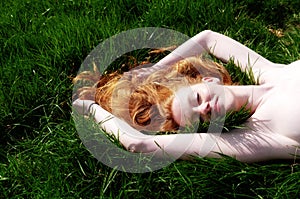 Beautiful Portrait of a young red-haired woman, raising her arms, lying in the summer sun on the green grass, the red hair