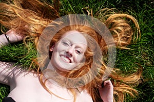 Beautiful portrait of a young sexy red-haired woman, laughing, lying in the spring, summer sun, relaxing on the green meadow grass