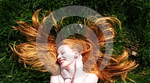 Beautiful portrait of a young sexy red-haired woman, lying in the summer sun in happiness, laughing, relaxing on the green grass,