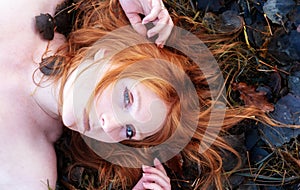 Beautiful Portrait of a young sexy red-haired woman, raising her arms, lying in the autumn sun, relaxing on the grass with autumn