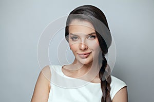 Beautiful positive brunette model woman with long dark hair and makeup smiling on gray background portrait