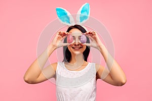 Beautiful and positive brunette woman in bunny ears and with painted Easter eggs pared eyes, easter