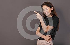 Beautiful positive business happy woman in black t-shirt showing the finger on empty copy space grey background