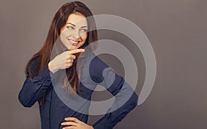 Beautiful positive business happy woman in blue shirt looking back side and showing the finger on empty copy space grey background