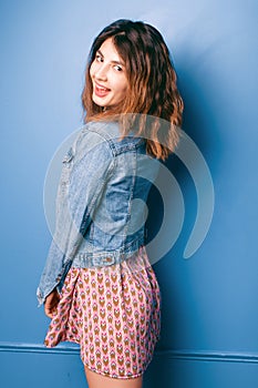Beautiful positive girl in a jeans jacket on a blue background smiling and posing