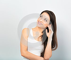 Beautiful positive young happy woman with hand under the face thinking and looking up in casual white t-shirt and long hair on