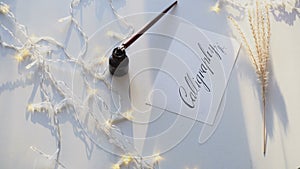 Beautiful postcard with calligraphic inscription of black ink on white sheet of paper among garland on light table.