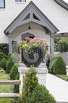 Beautiful pot of pink geraniums sitting on a fence post in front of a neatly landscaped white painted brick house entrance with