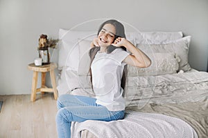 Beautiful pre-teen girl in casual clothes do stretching exercises seated on bed in cozy bedroom in the morning