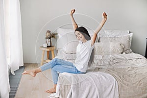 Beautiful pre-teen girl in casual clothes do stretching exercises seated on bed in cozy bedroom in the morning