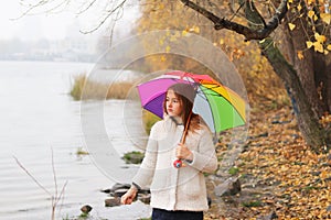 Beautiful pre-teen girl standing in the autumn park with bright colorful rainbow umbrella