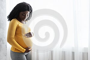 Beautiful pregnant african woman hugging her tummy at home