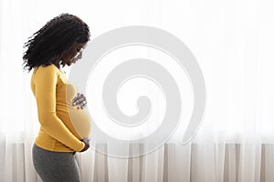 Beautiful pregnant black woman hugging her tummy at home