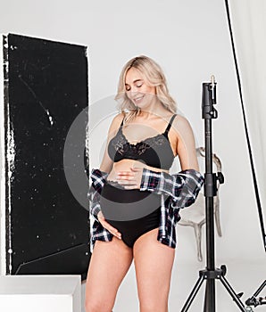 Beautiful pregnant blonde woman in underwear at a photo session in the studio with equipment for high-quality and beautiful