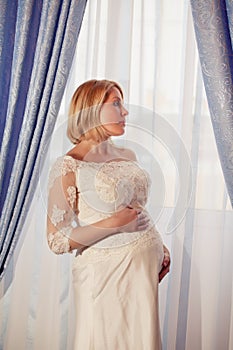 Beautiful pregnant bride posing against window