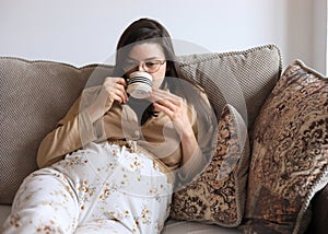 Beautiful pregnant Caucasian woman drinking tea while sitting on a couch