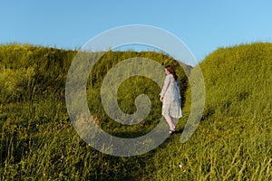 Beautiful pregnant girl dancing during sunset in a green field, a woman having fun and smiling