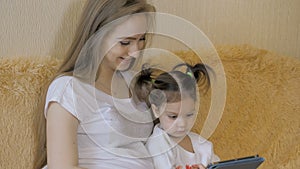 Beautiful pregnant girl and her cute little daughter are using a digital tablet