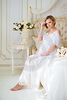 Beautiful pregnant girl in a home clothes sitting in the interior on a bed of roses