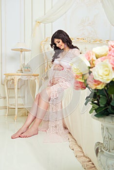 Beautiful pregnant girl in a lace negligee sitting on a bed of roses