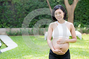 Beautiful pregnant of portrait asian young woman relax in the park, girl with belly standing on grass