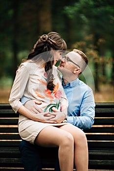 Beautiful pregnant stylish couple relaxing outside in the autumn park sitting on bench.