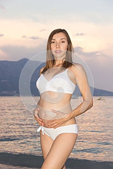 A beautiful pregnant woman on the beach touching her belly