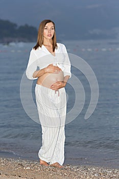 A beautiful pregnant woman on the beach touching her belly