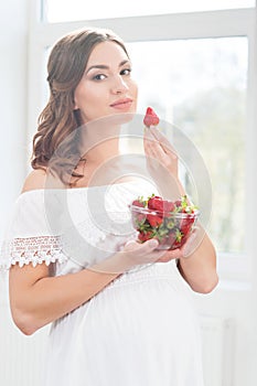 Beautiful pregnant woman with a bowl of strawberries