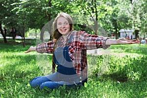 Beautiful pregnant woman in denim overalls sitting on the grass in the park