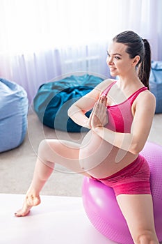 Beautiful pregnant woman doing exercises on a fitness ball. Expectant mother in the last trimester doing yoga.