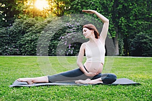 Beautiful pregnant woman doing prenatal yoga on nature outdoors.