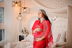 Beautiful pregnant woman dressed in elegant red negligee