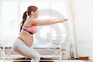 Beautiful pregnant woman excercising in a bright room