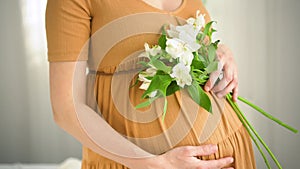 Beautiful pregnant woman with flowers in hand strokes her belly. The concept of a happy pregnancy.