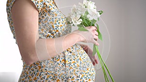 Beautiful pregnant woman with flowers in hand strokes her belly. The concept of a happy pregnancy.