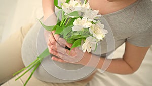 Beautiful pregnant woman with flowers in hand strokes her belly. The concept of a happy pregnancy.