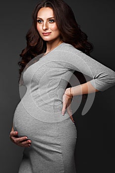 Beautiful pregnant woman in a gray dress, with a classic make up and curls. Beauty face.