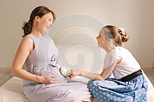 Beautiful pregnant woman and her cute little daughter are smiling while spending time together at home.