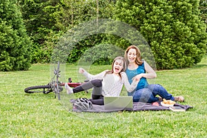 Beautiful pregnant woman and her daughter are laughing in a summer green park with laptop and bicycle.