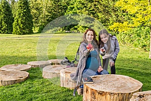 Beautiful pregnant woman and her daughter in a summer green park holding apple and cherry