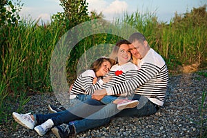 Beautiful pregnant woman with her family sitting by the river.