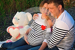 Beautiful pregnant woman with her family sitting by the river.