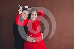 Beautiful pregnant woman with her husband holding baby booties, posing in studio