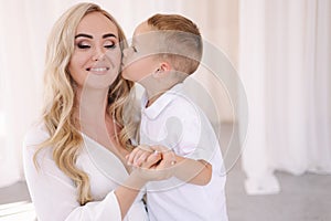 Beautiful pregnant woman with her son. Boy kiss her mom in cheek. Lady in elegant white dress posing to photographer in