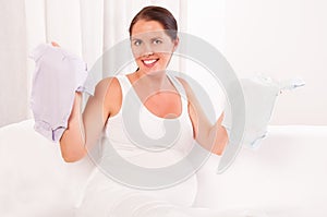 Beautiful pregnant woman holding baby clothes- bodysuits photo