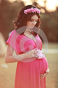 Beautiful pregnant woman holding baby's bootee over nature park