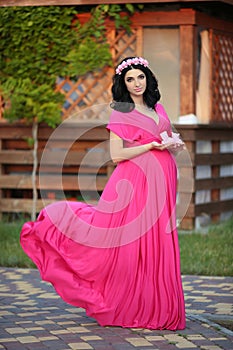 Beautiful pregnant woman holding baby's bootee wearing in pink d